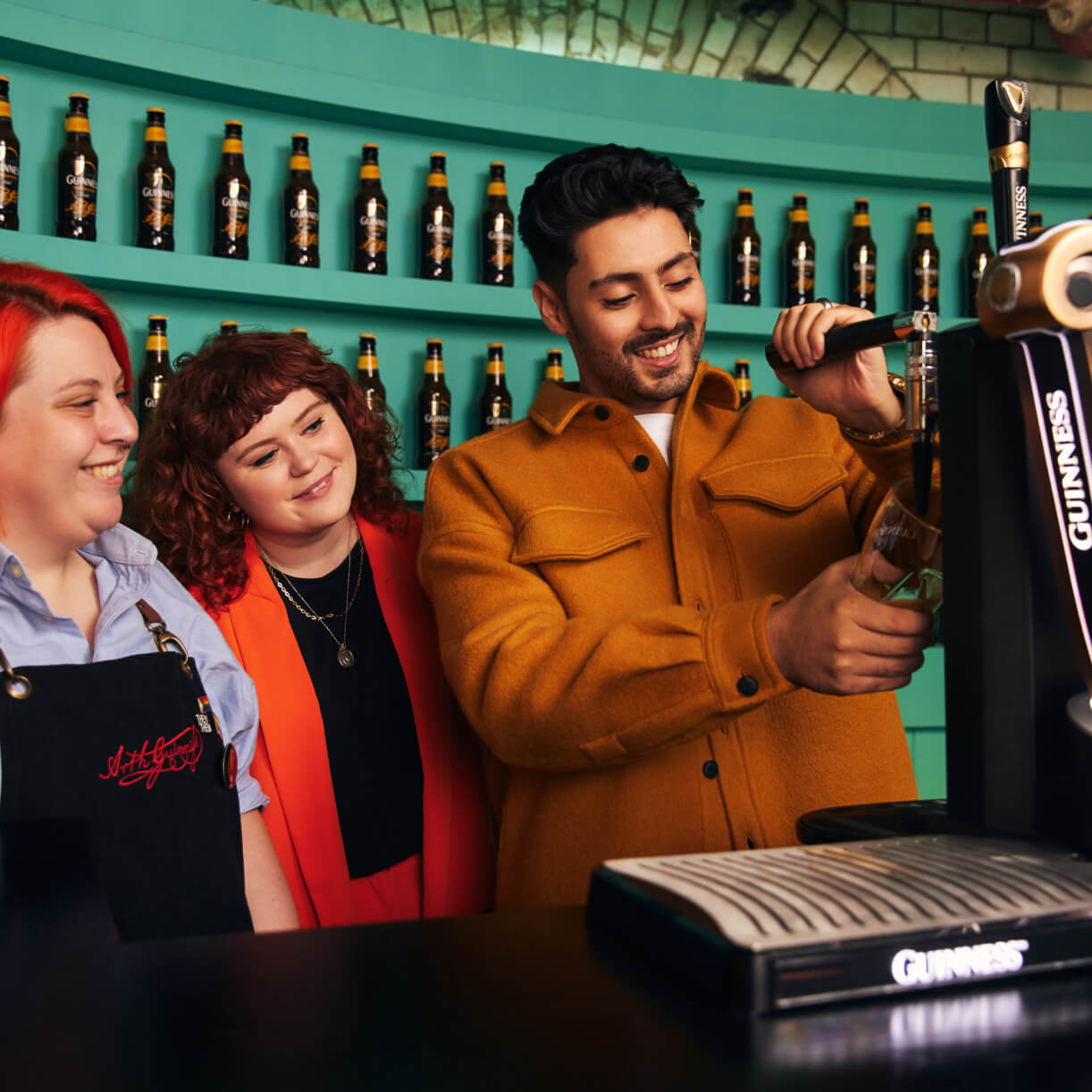 Guinness Storehouse staff member and woman proudly watching a happy man pulling his own pint of Guinness