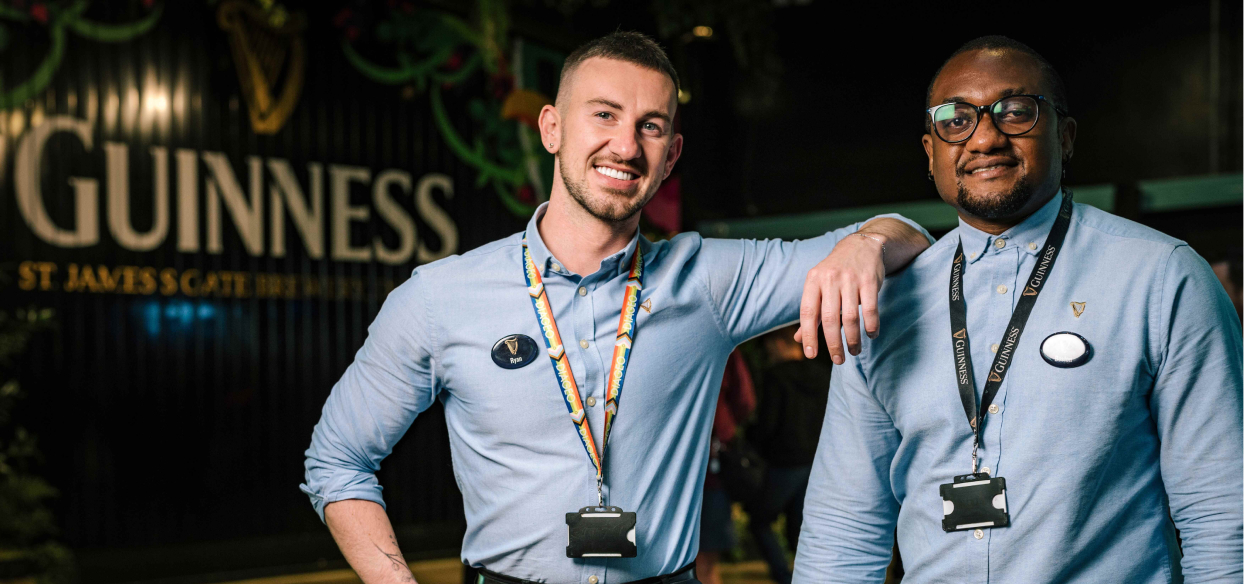Two happy male tour guides standing inside the Guinness Storehouse